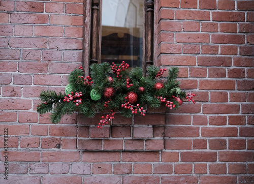 Window in an old brick building. Decoration for Christmas and New Year. Green branches, red balls.