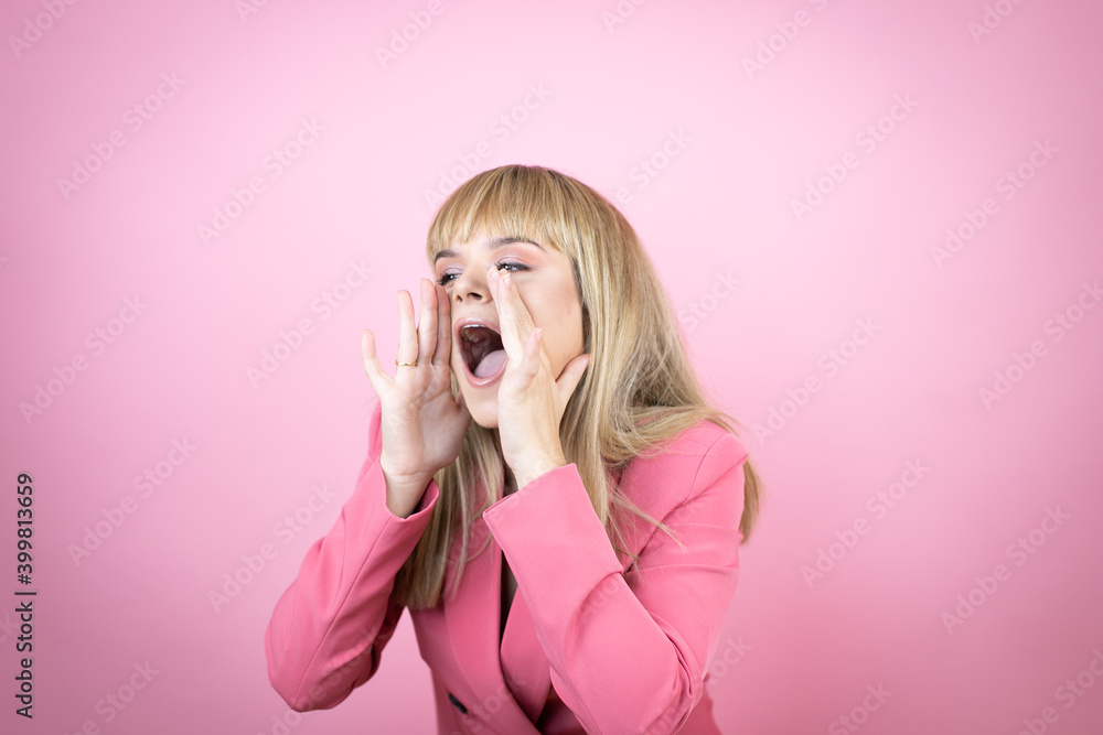 Young caucasian woman over isolated pink background shouting and screaming loud to side with hands on mouth Young caucasian woman over isolated pink background shouting and screaming loud to side with hands on mouth
