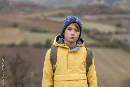 Serious little boy with a backpack on a hill in autumn day.