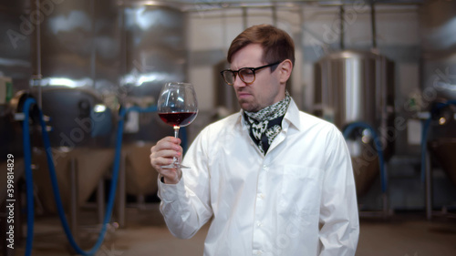 Fotografija Man sommelier in lab coat tasting wine at modern wine factory