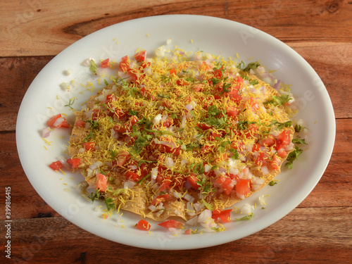 Masala Papad is a delicious Indian snack made using roasted or fried papad topped with a tangy and spicy onion tomato mix, served over a rustic wooden background, selective focus photo