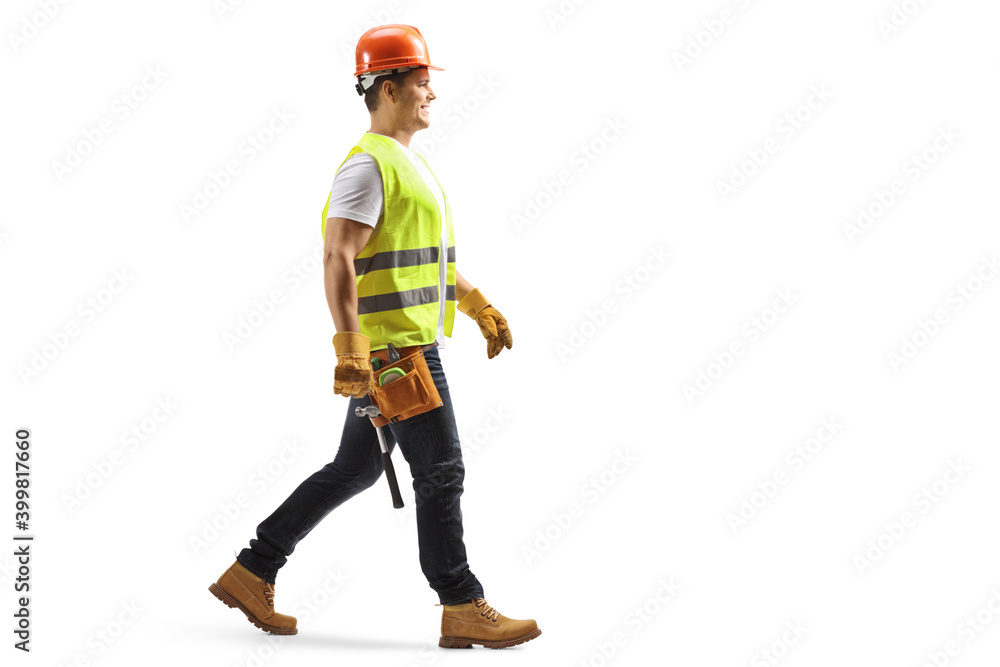 Full length profile shot of a construction worker with a helmet and tool belt walking Full length profile shot of a construction worker with a helmet and tool belt walking