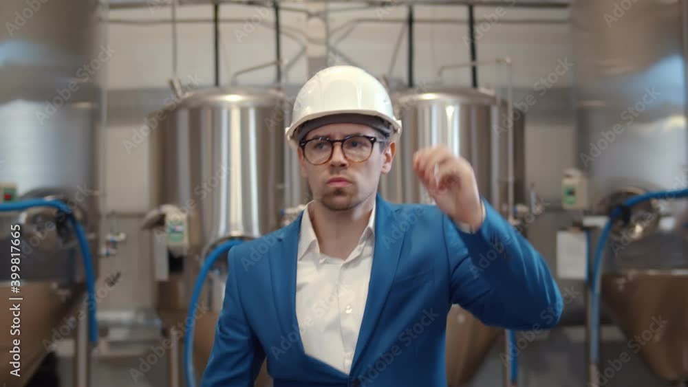 Portrait of serious businessman in hardhat walking in modern brewery workshop Portrait of serious businessman in hardhat walking in modern brewery workshop