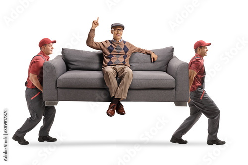 Movers carrying an elderly man sitting on a sofa and pointing up photo