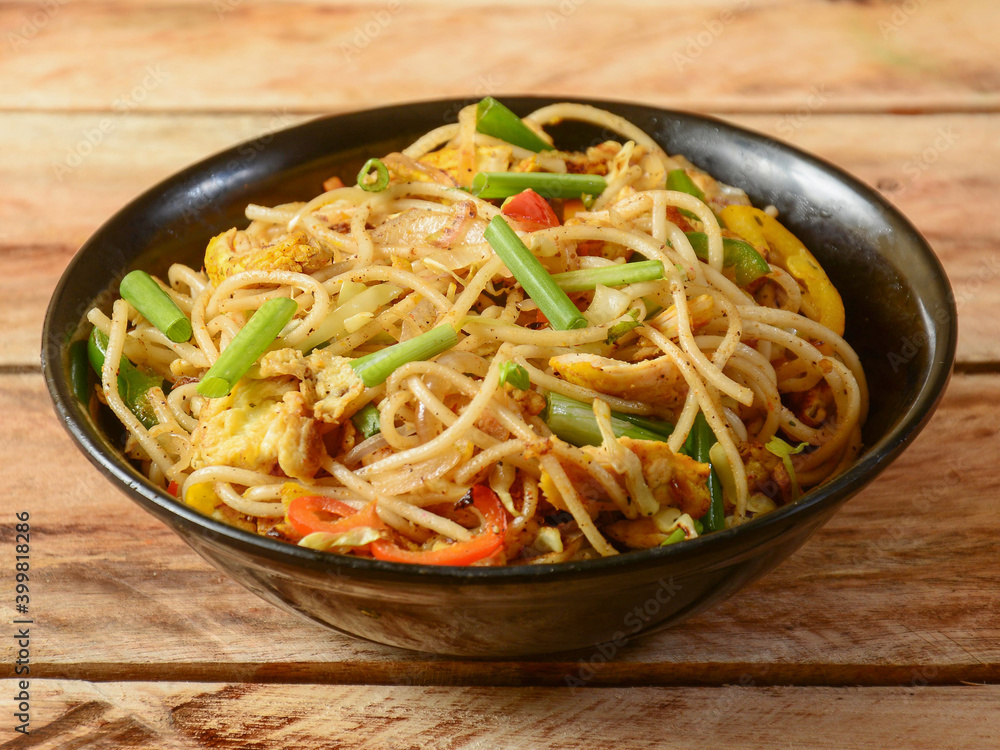 Chicken chow mein a popular oriental dish with noodles and vegetables, served over a rustic wooden background, selective focus Chicken chow mein a popular oriental dish with noodles and vegetables, served over a rustic wooden background, selective focus