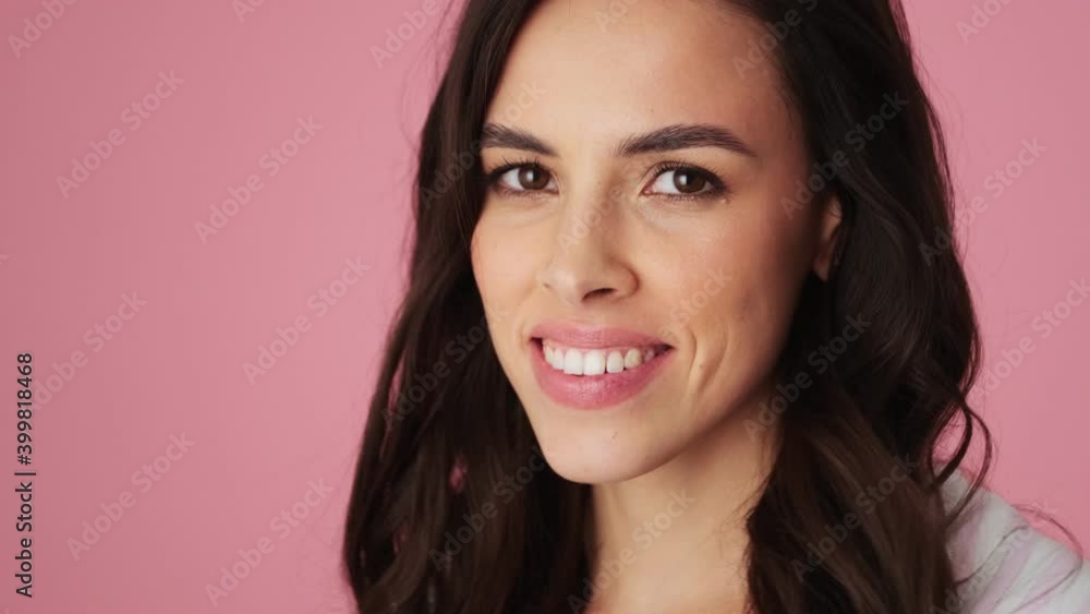 A close-up view of a pretty nice young woman is doing secret gesture standing isolated over a pink background in the studio A close-up view of a pretty nice young woman is doing secret gesture standing isolated over a pink background in the studio