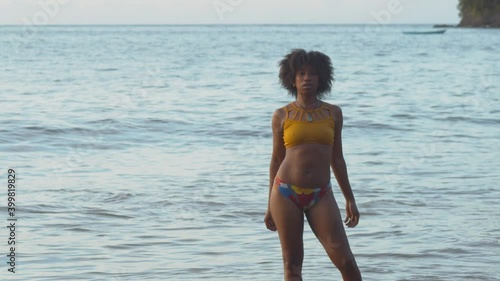 A sexy black girl stands in the ocean with a fishing boat in the background on the Caribbean island of Trinidad photo