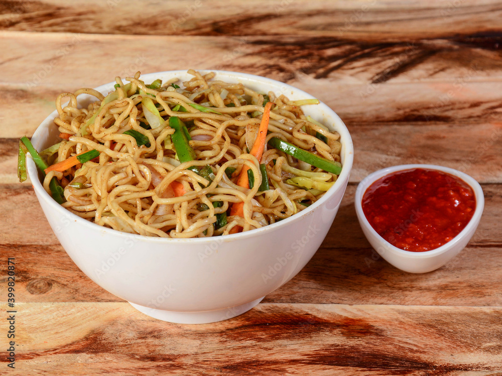 Veg Hakka Noodles a popular oriental dish made with noodles and vegetables, served over a rustic wooden background, selective focus Veg Hakka Noodles a popular oriental dish made with noodles and vegetables, served over a rustic wooden background, selective focus