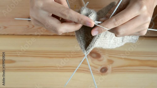 young womans hands knitting with gray metal needles and woolen thread on wooden table background, top view close-up full HD stock video footage in real-time