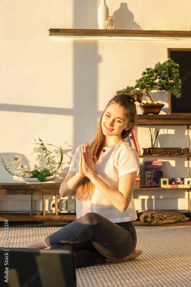 Young attractive woman practicing yoga,sitting in Lotus position and greeting her colleagues in front of laptop screen at home.Fitness and Yoga online training concept in the  coronavirus pandemic.