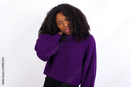 Young beautiful African American woman wearing knitted sweater against white wall,  Suffering of neck ache injury, touching neck with hand, muscular pain © Roquillo