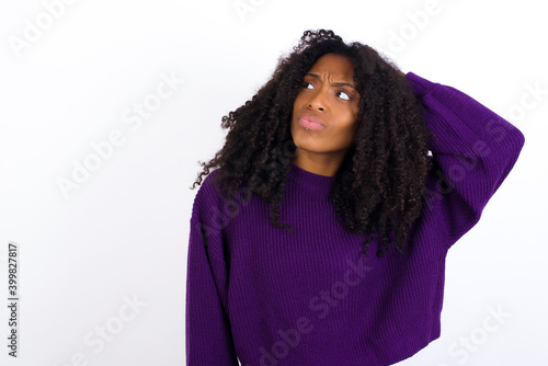 Young beautiful African American woman wearing knitted sweater against white wall,  confuse and wonder about question. Uncertain with doubt, thinking with hand on head. Pensive concept. © Roquillo