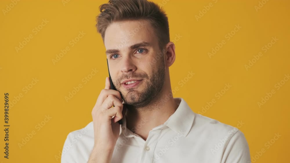 Handsome young cheerful man talking by mobile phone isolated over yellow wall background Handsome young cheerful man talking by mobile phone isolated over yellow wall background