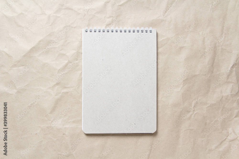 Gray notepad with white coiled spring on a background of beige crumpled craft paper Gray notepad with white coiled spring on a background of beige crumpled craft paper