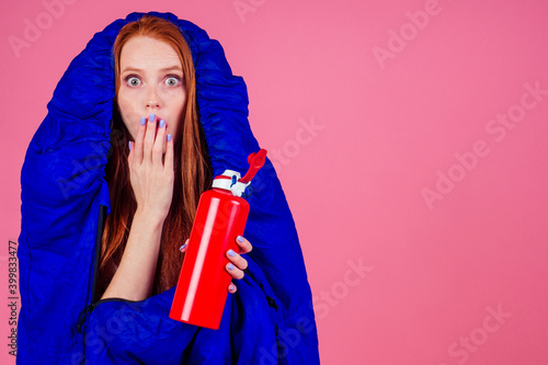 redhair ginger woman holding red thermos and wrapped in in sleeping bag photo