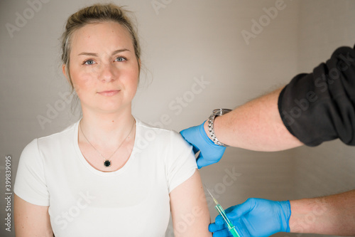 Doctor injecting Covid Vaccine into a young blonde womans arm: Curing the Corona Pandemic with mass Vaccination