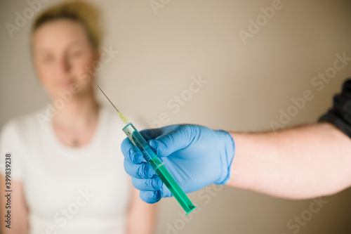 Doctor holding a Covid Vaccine in his hands with young blonde female patient in the background  Curing the Corona Pandemic with mass Vaccination