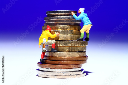 conceptual image of miniature figure people climbing a stack of coins to reach thier monetory goal photo