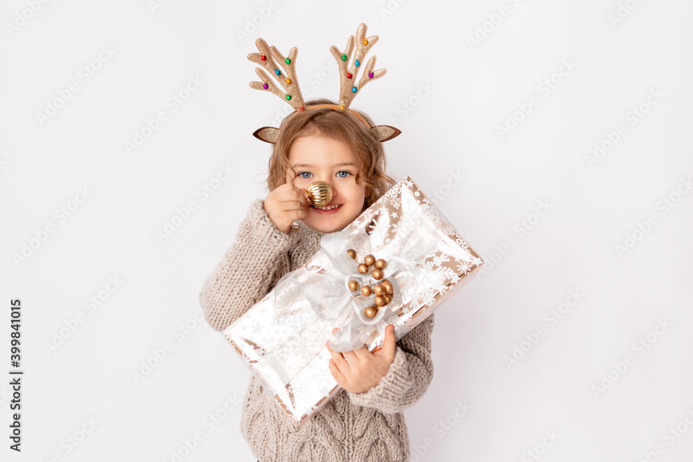little girl with deer antlers and Christmas ball on her nose on a white background with a gift in her hands, space for text, new year and Christmas concept little girl with deer antlers and Christmas ball on her nose on a white background with a gift in her hands, space for text, new year and Christmas concept