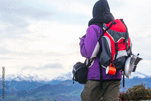 hiker equipped with warm clothing, backpack and camping utensils, replenishes energy while observing the snowy mountain range. Winter sports.