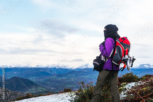 mountaineer with a covered head and warm clothes resting and contemplating the beautiful landscape of the snowy mountains. adventure and free time concept.