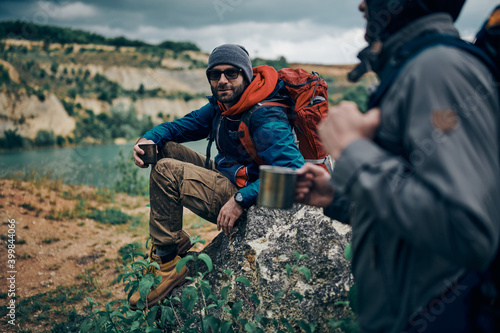 Two men in nature taking a break from hiking. They refreshing and drinking hot tea.