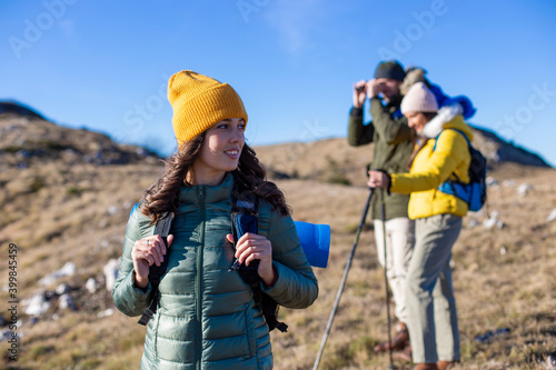 Portrait of a smiling woman hiking at the top of the mountain. A Group of friends is enjoying the fresh air and sun. 