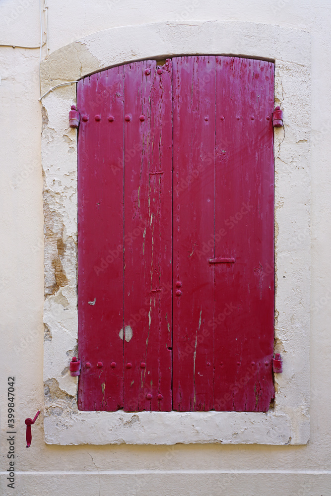 Red window shutters closed on a colorful wall in France