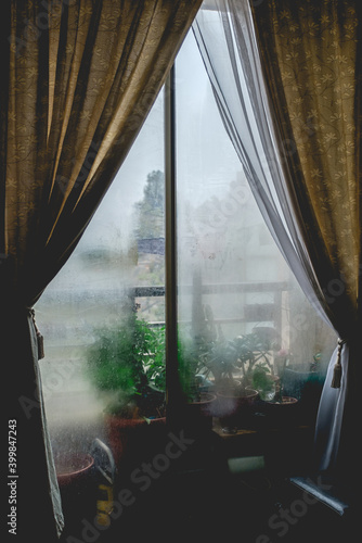 Foggy windows in a rainy day with a balcony with green plants and curtains