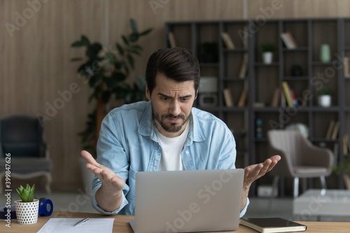 Cuadro en lienzo Unhappy young Caucasian man sit at desk at home look at laptop screen frustrated by gadget problem