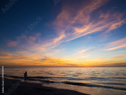 Young woman walking on a Gulf of Mexico beach at St. Pete Beach, Florida at sunset with a dramatic orange sunlit sky.