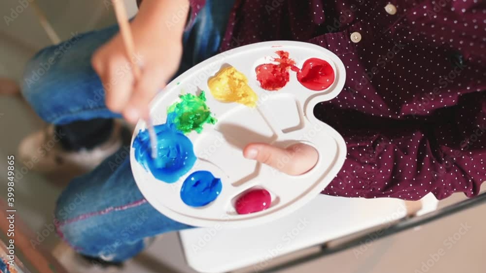Boy draws a rainbow on canvas in self-isolation. He holds a brush in his hand, makes blue paint. The creative manifestation of the child in the lesson. Boy draws a rainbow on canvas in self-isolation. He holds a brush in his hand, makes blue paint. The creative manifestation of the child in the lesson.