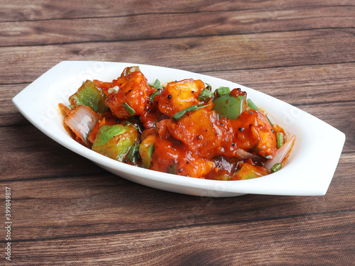 Paneer Manchurian is Indo Chinese cuisine dish, Paneer cubes tossed with tomatoes, onions, spring onions, sesame seeds and soy sauce. served over a rustic wooden background, selective focus