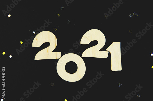 Wooden numbers 2021 on a black background with yellow and gray glitter stars.