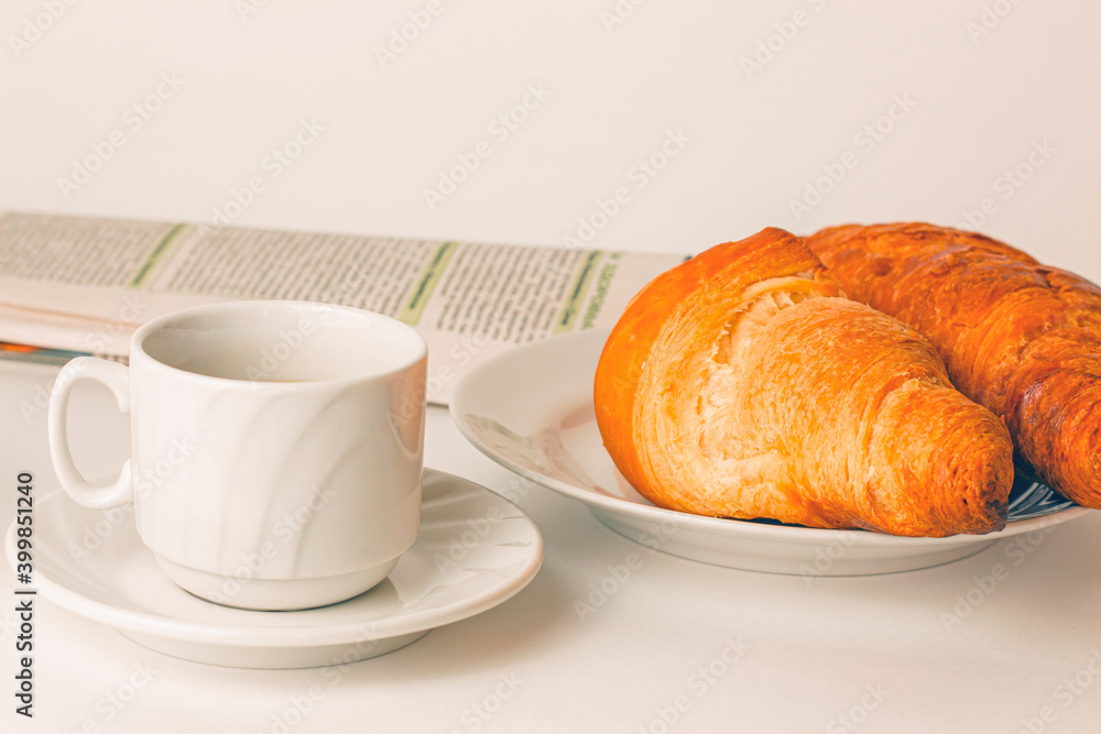 breakfast: a cup of coffee, two croissants on a plate and a morning newspaper on the table breakfast: a cup of coffee, two croissants on a plate and a morning newspaper on the table