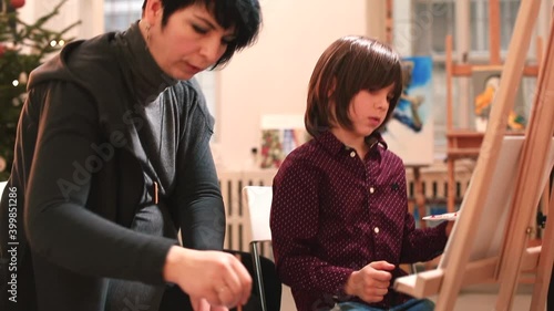 An art teacher assists a child in an art school. The boy makes a drawing sitting in front of a malbert. They are discussing work. Finger holding technique. photo
