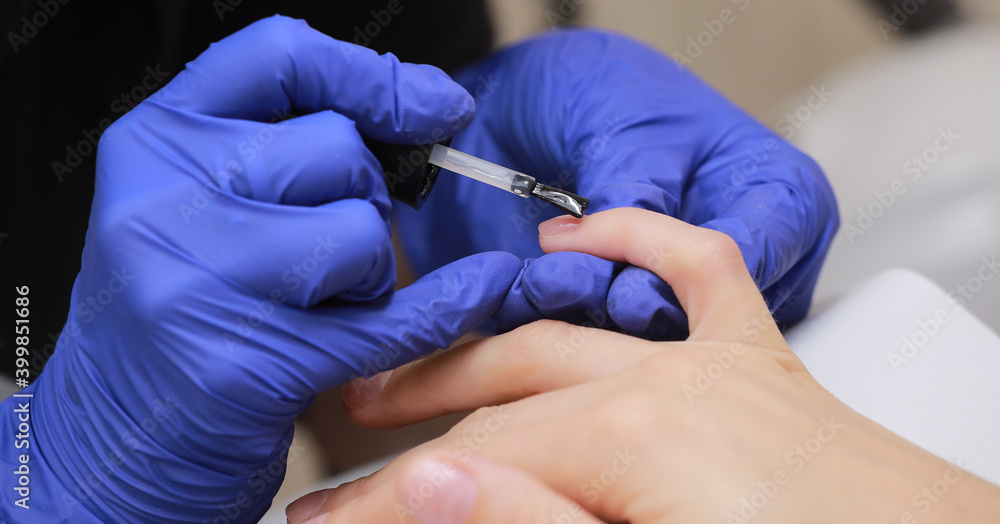 Closeup shot of manicure in a beauty salon. Master during a manicure. Master manicurist varnishes the gel on the nails of a female client. The concept of beauty and health. Closeup shot of manicure in a beauty salon. Master during a manicure. Master manicurist varnishes the gel on the nails of a female client. The concept of beauty and health.