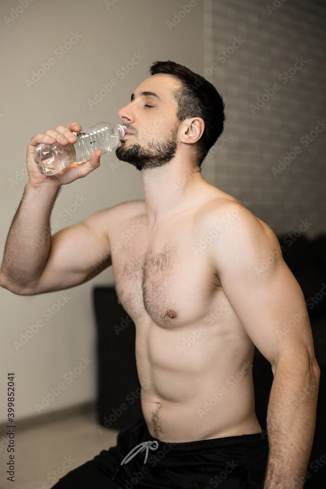 Topless attractive man drinking water after hard workout at home. Resting time. Sporty muscular man drinking water after exercising. Bodybuilding workout. Hydration and fitness concept. Topless attractive man drinking water after hard workout at home. Resting time. Sporty muscular man drinking water after exercising. Bodybuilding workout. Hydration and fitness concept.