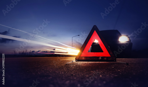 Red emergency stop sign (red triangle warning sign) with long-exposure of traffic light trails at nigh.