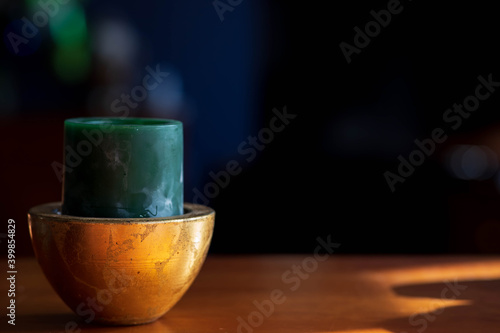 Dark blue green unlit candle in a crackled gold candle holder placed on a dark cherry desk with a dark background
