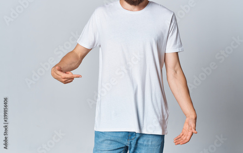 A man in a white T-shirt on a light background gestures with his hands cropped view of jeans Copy Space