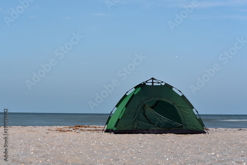 Green tent on sandy beach against sea and blue sky background. Camping, active tourism