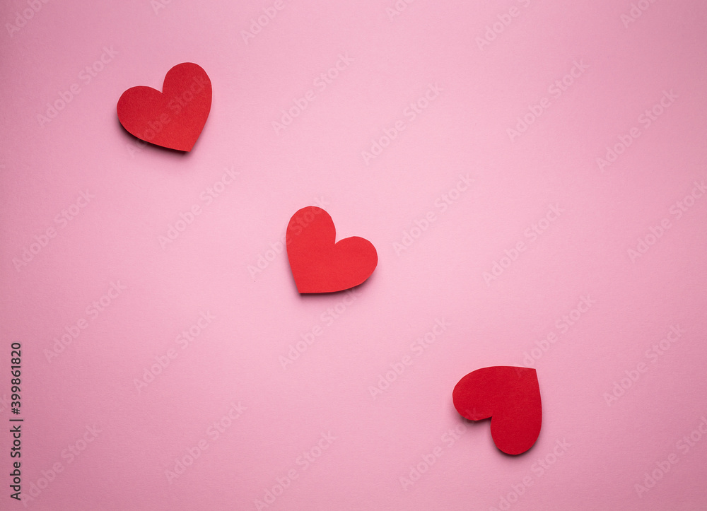 Three red hearts in a row cut from paper on pink background, craft origami style, from above. Romantic Valentine's day love concept. Different size hearts top view, paper art design 
