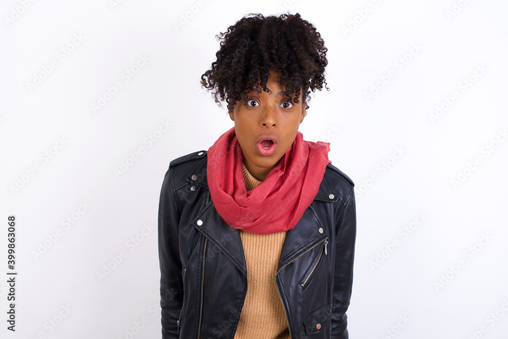 Young beautiful African American woman wearing biker jacket having stunned and shocked look, with mouth open and jaw dropped exclaiming: Wow, I can't believe this. Surprise and shock Young beautiful African American woman wearing biker jacket having stunned and shocked look, with mouth open and jaw dropped exclaiming: Wow, I can't believe this. Surprise and shock