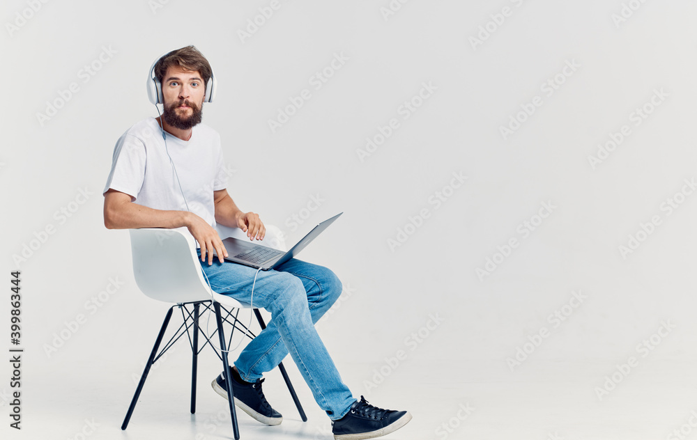 man in headphones with laptop on his knees sitting on chair communication isolated background