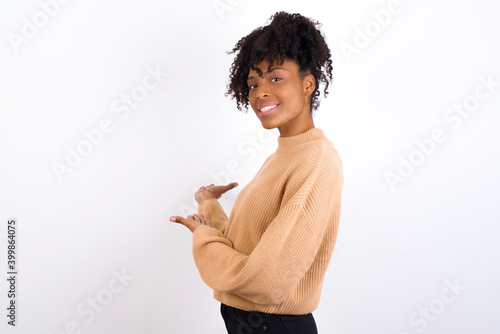 Young beautiful African American woman wearing knitted sweater against white wall Inviting to enter smiling natural with open hands. Welcome sign.