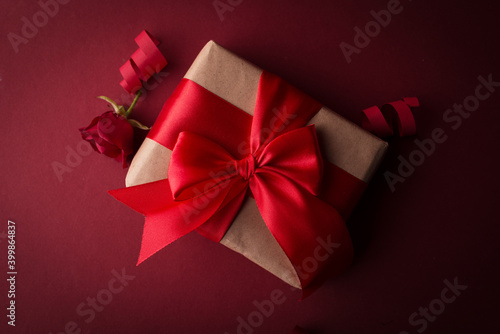 Close up Gift box with red silk bow against dark purple background. Valentines day romantic gift box with red rose. 14 February background.