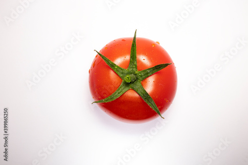 Close up view of tomato isolated on a white background with water drops on surface green stem top side. Space for copy 