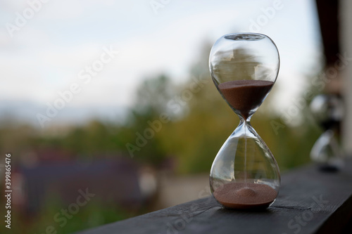 Hourglass on a wood table with green forest and sun light background