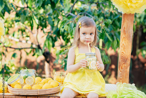 Child Girl drink natural lemonade at stand in park. Summer refreshing natural drink lemonade. Detox fruit infused flavored water, cocktail in a beverage dispenser with fresh fruits